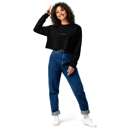 Nainen mustassa cropped collegepaidassa, jossa Make It Happen -painatus. Rennon tyylikäs ja minimalistinen streetwear-look yhdistettynä farkkuihin ja tennareihin.